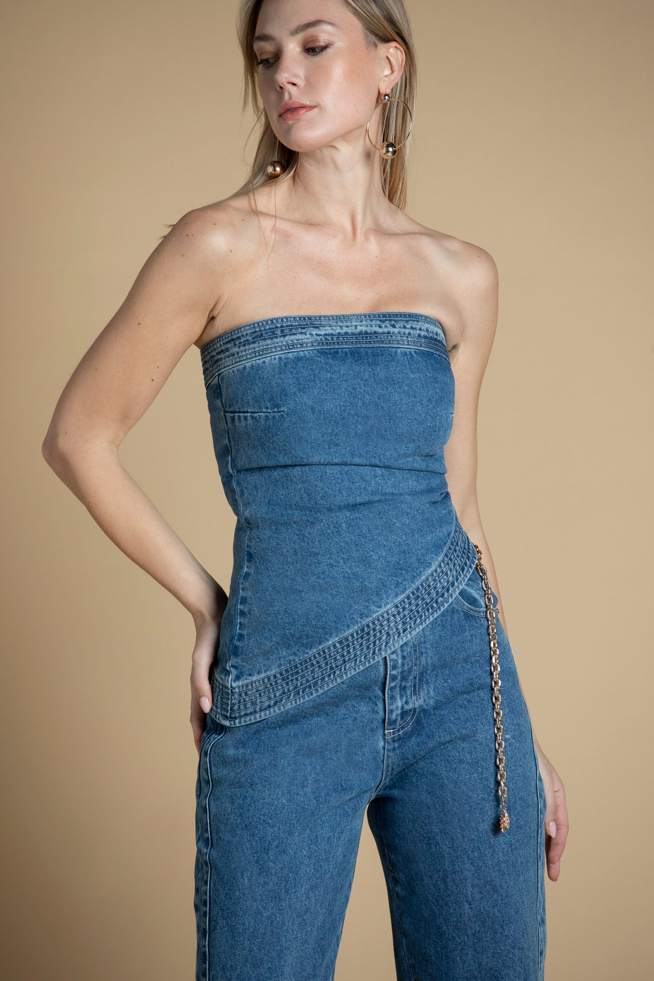 Vista frontal do top bandeau em denim, com decote direito e ombros descobertos, revelando o corte assimétrico de inspiração contemporânea.