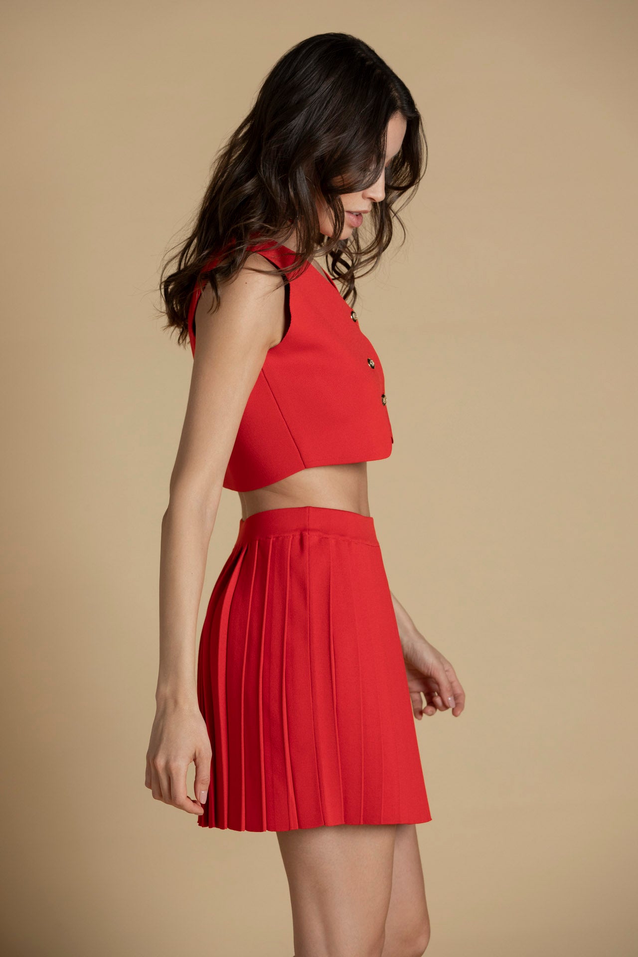 Perfil do top vermelho em malha com botões dourados em destaque e estrutura ajustada.